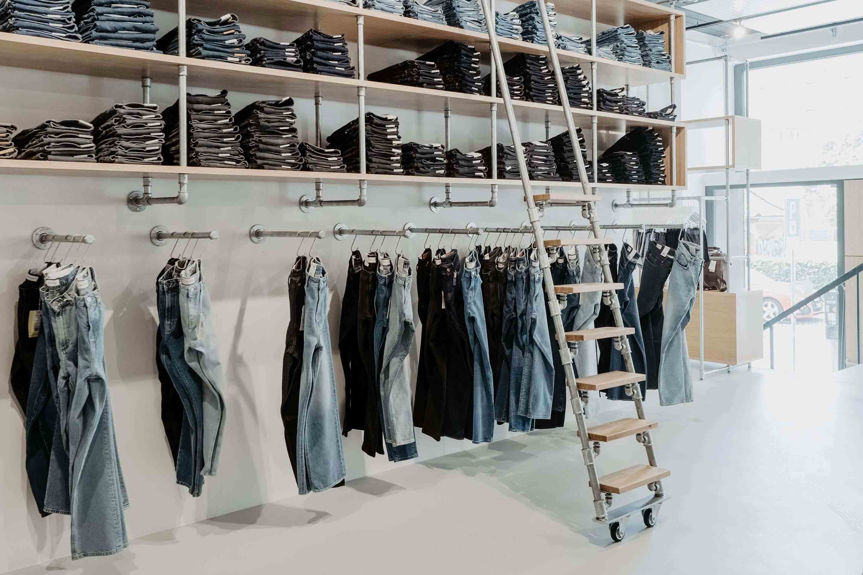 Jeansregal zieht sich über eine gesamte Wand und präsentiert hängend und gestapelt verschiedene Jeansmodelle unterschiedlichster Waschung und Farbe