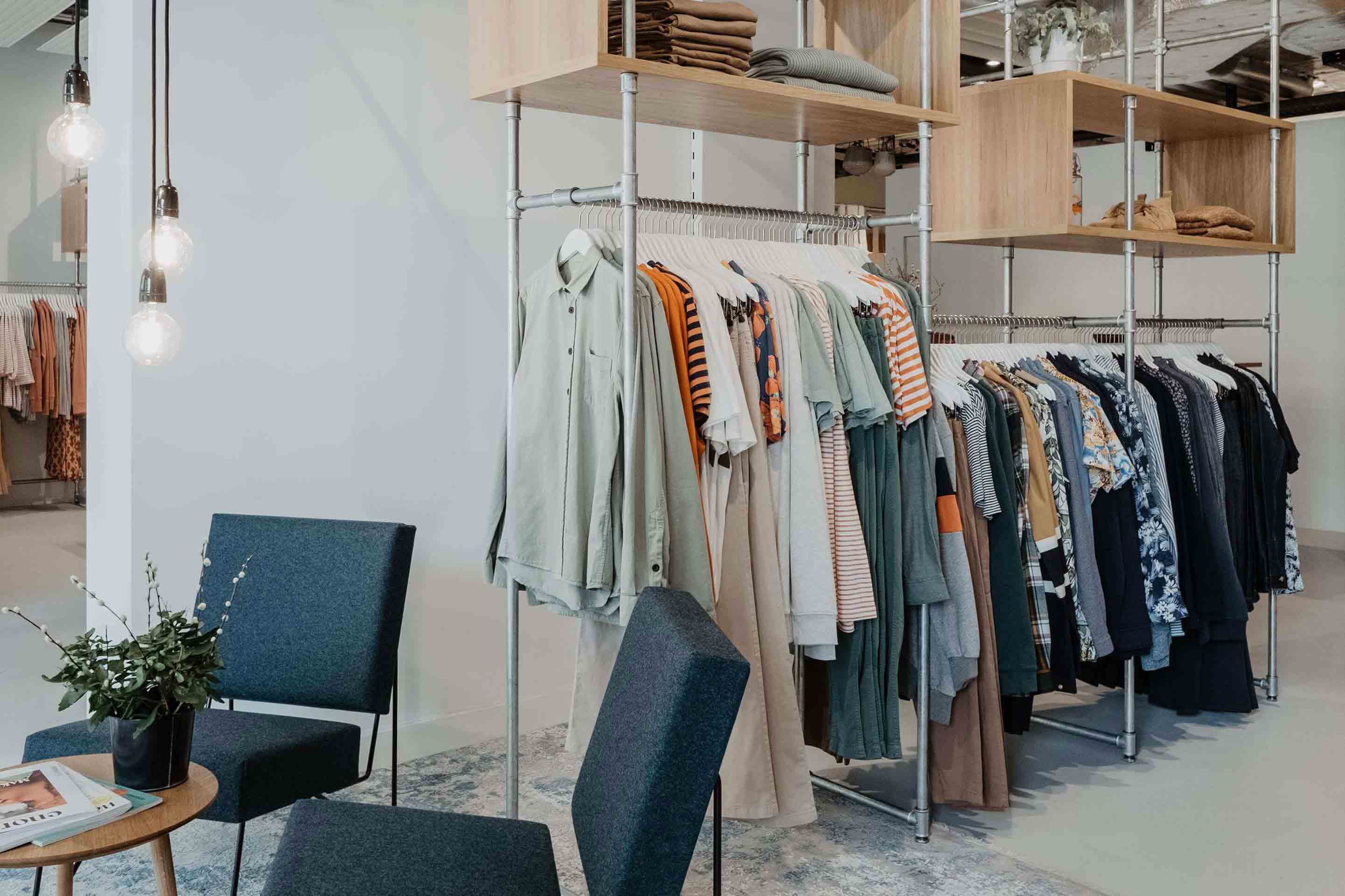 Gemütlicher Wartebereich mit Sesseln und kleinem Tisch neben Kleiderstangen und Regalen mit nachhaltiger Mode für Männer im glore Laden in Zürich
