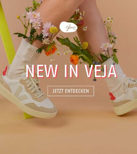 Der Veja V-90 angezogen, vor orangenem Hintergrund mit Blumen in den Socken mit der Aufschrift New In Veja.
